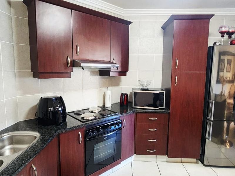A functional kitchen featuring dark wood cabinetry, granite countertops, a double basin sink, and built-in cooking appliances with a tiled backsplash.