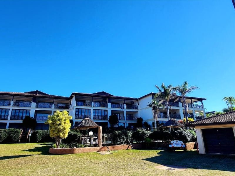A wide-angle view of the apartment complex rear facade, featuring multi-level balconies with wrought iron railings, a well-maintained garden, and attached garage units.