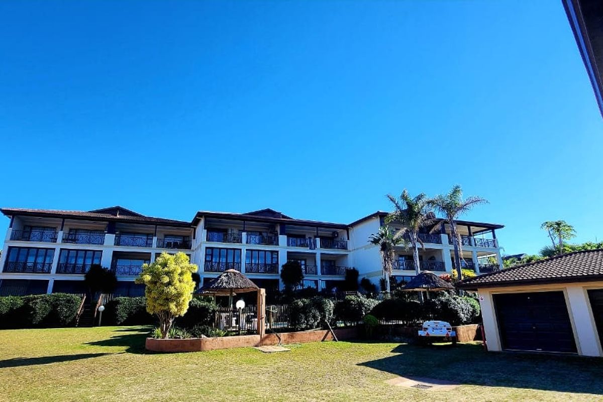 A wide-angle view of the apartment complex rear facade, featuring multi-level balconies with wrought iron railings, a well-maintained garden, and attached garage units.