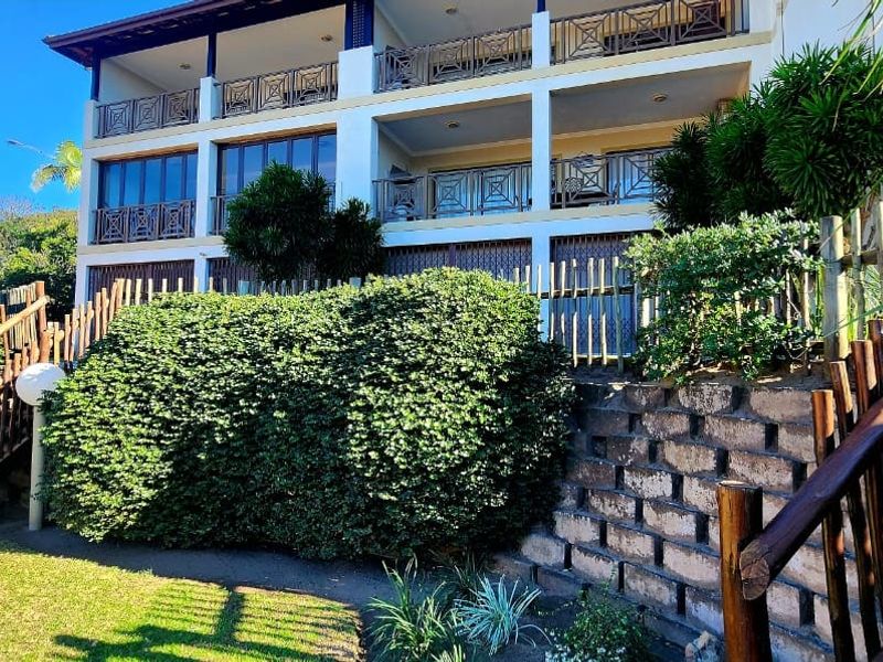 Rear view of a multi-story apartment building featuring tiered balconies, timber staircases, and a landscaped garden with a retaining wall.