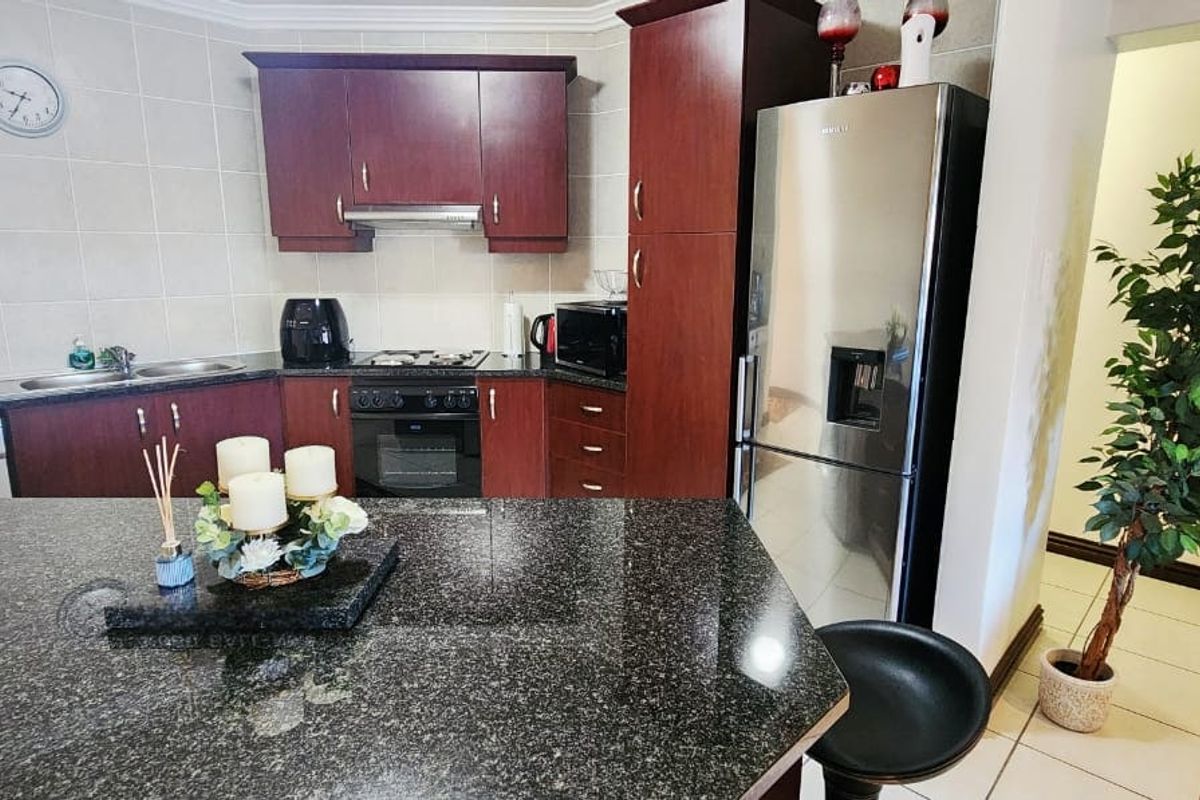 A functional kitchen featuring dark wood cabinetry, granite countertops, a built-in oven with gas hob, and tiled flooring throughout.