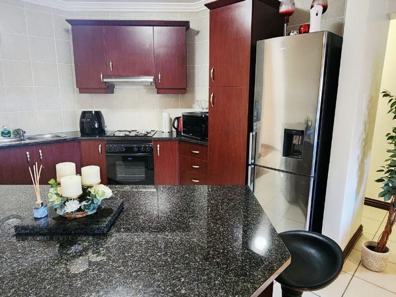 A functional kitchen featuring dark wood cabinetry, granite countertops, a built-in oven with gas hob, and tiled flooring throughout.