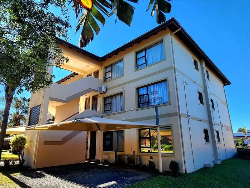 Exterior view of a multi-story apartment building featuring a paved driveway, shade sail parking, and external staircase access.