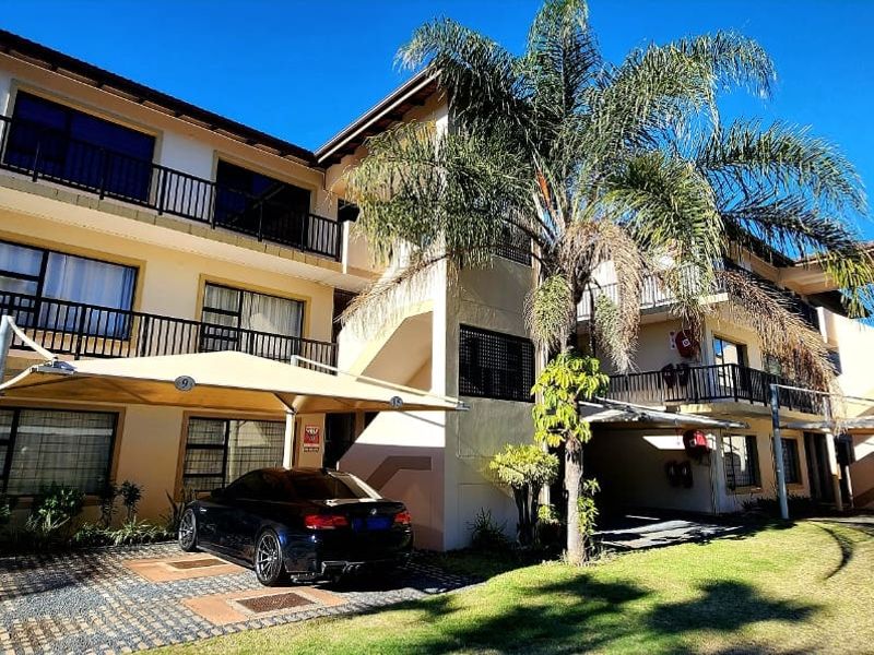 Exterior view of a multi-story apartment complex featuring paved parking bays with shade sails, private balconies, and well-maintained landscaped grounds.