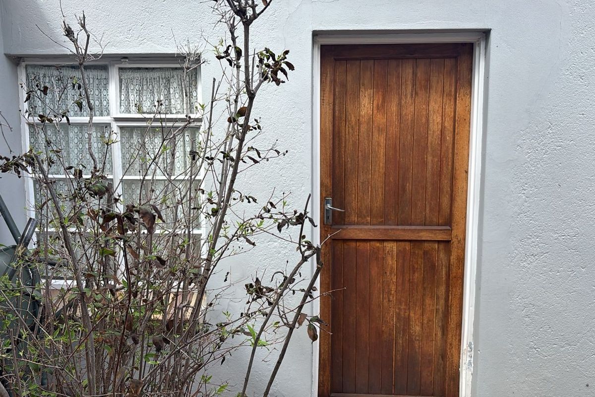 A view of a rear exterior wall featuring a timber door and a multi-pane window set into a plastered facade.