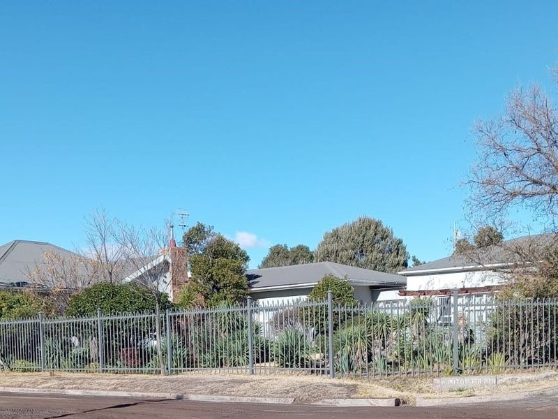 A street-level view of the property featuring a metal perimeter fence, tiled roof, and established garden area.