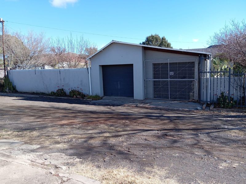 A detached garage structure featuring a roller shutter door and adjacent metal security gate, set behind a perimeter wall and fencing.