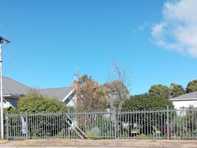 Front elevation of a residential property featuring a metal roof, established garden, and secure perimeter fencing.