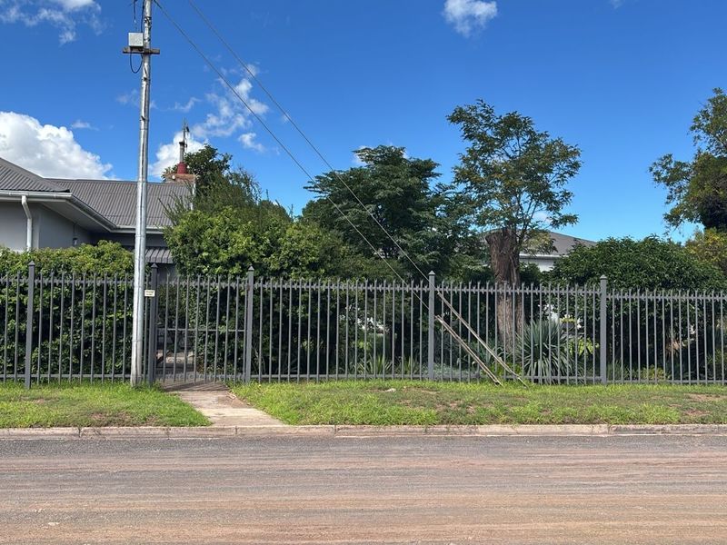 Street view of the property showing the front boundary with metal perimeter fencing, a pedestrian gate, and established garden landscaping.