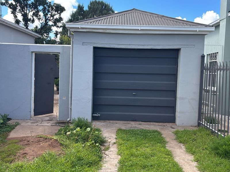 A detached single garage featuring a dark grey door, adjacent pedestrian gate, and metal perimeter fencing with a concrete driveway.
