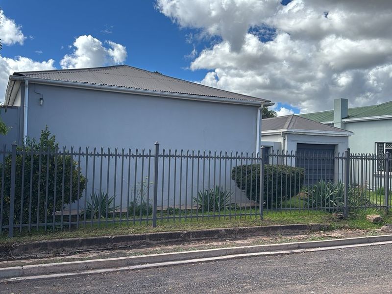Street view of the property featuring a metal security fence, concrete driveway, and a detached garage structure with a pitched roof.