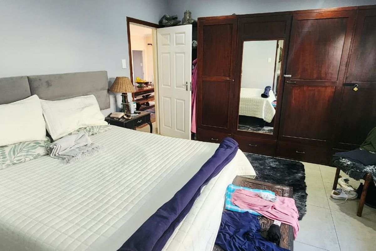 A bedroom featuring tiled flooring and a large built-in wooden wardrobe with a central mirror panel.
