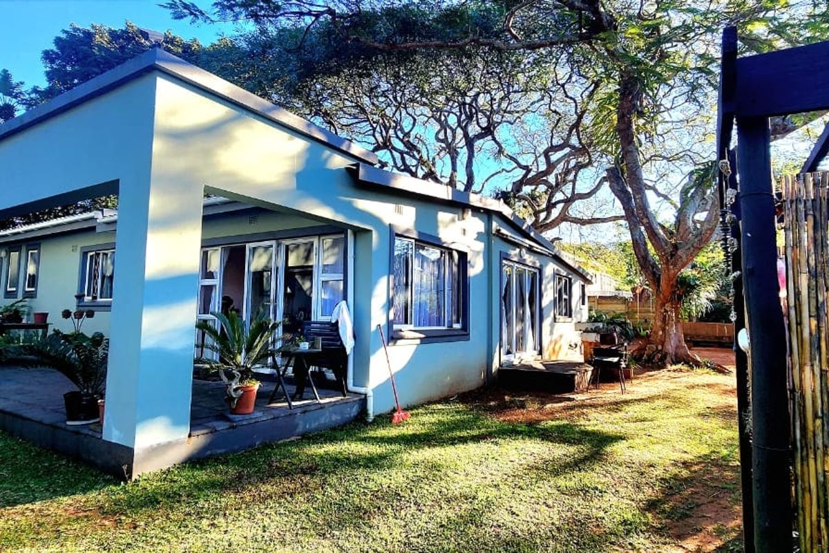 Rear view of the house featuring a spacious covered patio with sliding glass doors, overlooking a well-maintained garden area with mature trees.