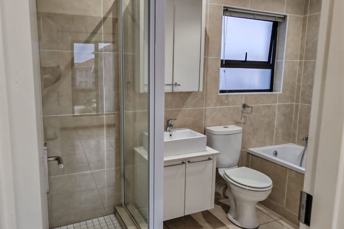 Modern bathroom featuring a glass shower enclosure, bathtub, vanity cabinet with basin, and neutral wall tiling.