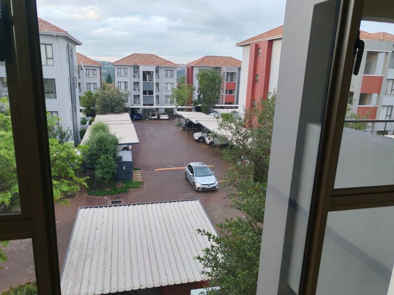 An elevated view overlooking the apartment complex courtyard, featuring paved parking areas, covered carports, and surrounding residential building blocks.