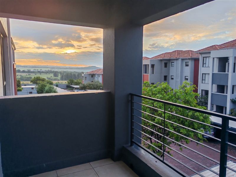 A covered balcony featuring tiled flooring and a metal balustrade, offering scenic sunset views over the surrounding estate and landscape.