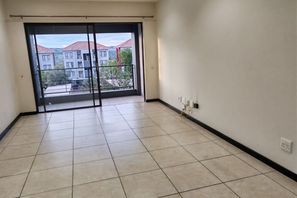 An empty, tiled living room featuring a large sliding glass door that opens onto a balcony, providing natural light and access to outdoor space.
