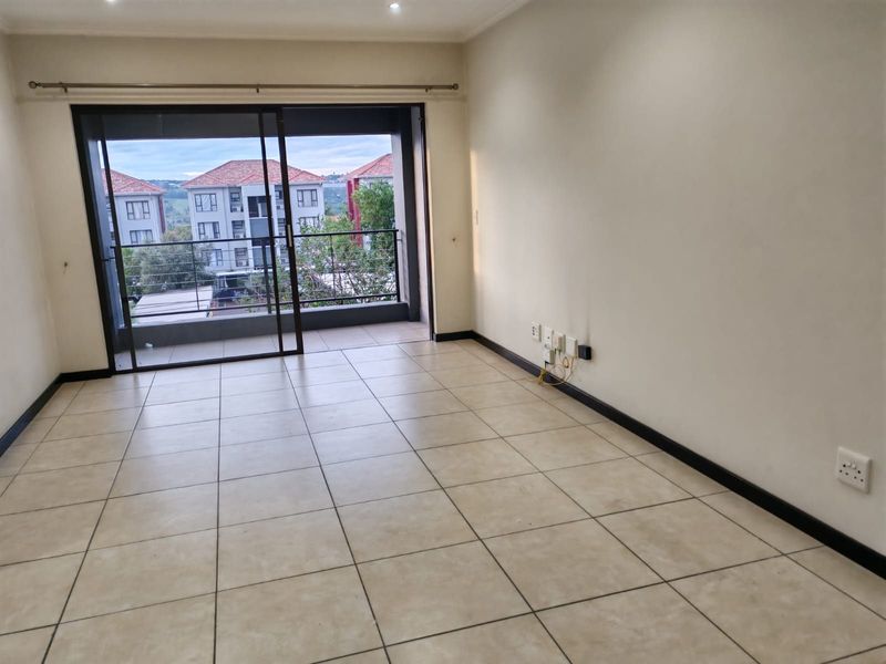 An empty, tiled living room featuring a large sliding glass door that opens onto a balcony, providing natural light and access to outdoor space.
