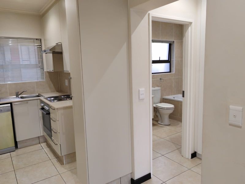 An open-plan kitchen featuring modern cabinetry and built-in appliances, with an adjacent bathroom visible through the doorway, both finished with neutral floor tiles.