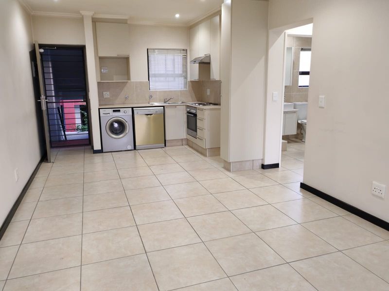 Open-plan kitchen and living area featuring tiled floors, built-in cabinetry, integrated appliances, and direct access to an exterior security gate.