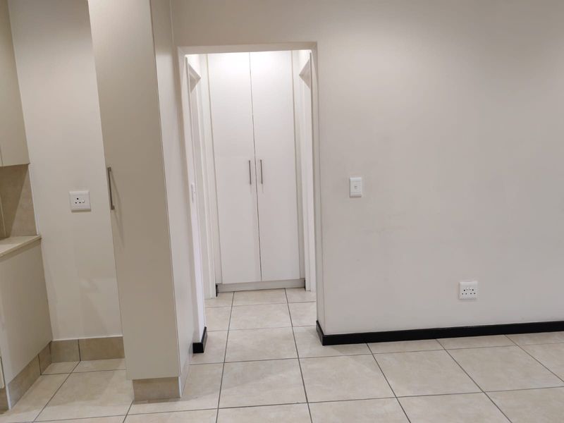 A clean, neutral hallway featuring tiled flooring and built-in storage cupboards, providing a bright and functional transition space within the apartment.