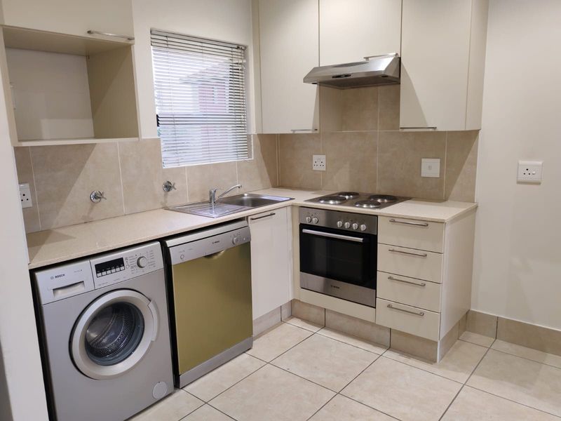 A well-maintained kitchen featuring built-in cabinetry, stone countertops, integrated oven and hob, extractor fan, and tiled finishes with space for under-counter appliances.