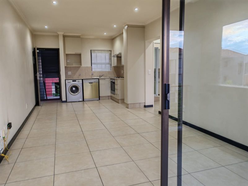 An open-plan kitchen and living area featuring tiled flooring, recessed lighting, and built-in cabinetry with integrated appliances, leading to a sliding glass door.