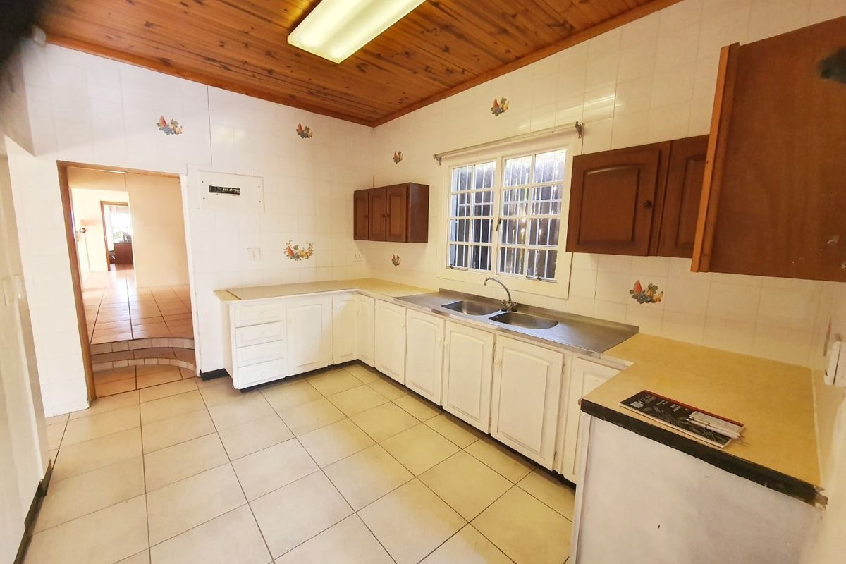 A dated kitchen featuring timber ceilings, tiled splashbacks, and built-in cabinetry with a double bowl stainless steel sink.