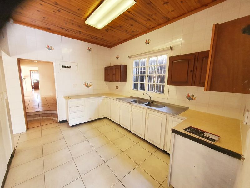 A dated kitchen featuring timber ceilings, tiled splashbacks, and built-in cabinetry with a double bowl stainless steel sink.