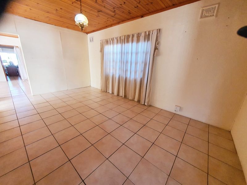 An empty living room featuring tiled flooring and a timber tongue and groove ceiling, offering a blank canvas for interior design.