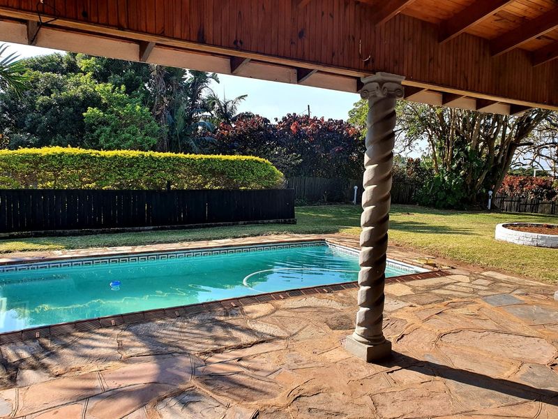 Outdoor pool area featuring a stone-paved patio, covered timber pergola, and a swimming pool set within a landscaped garden.