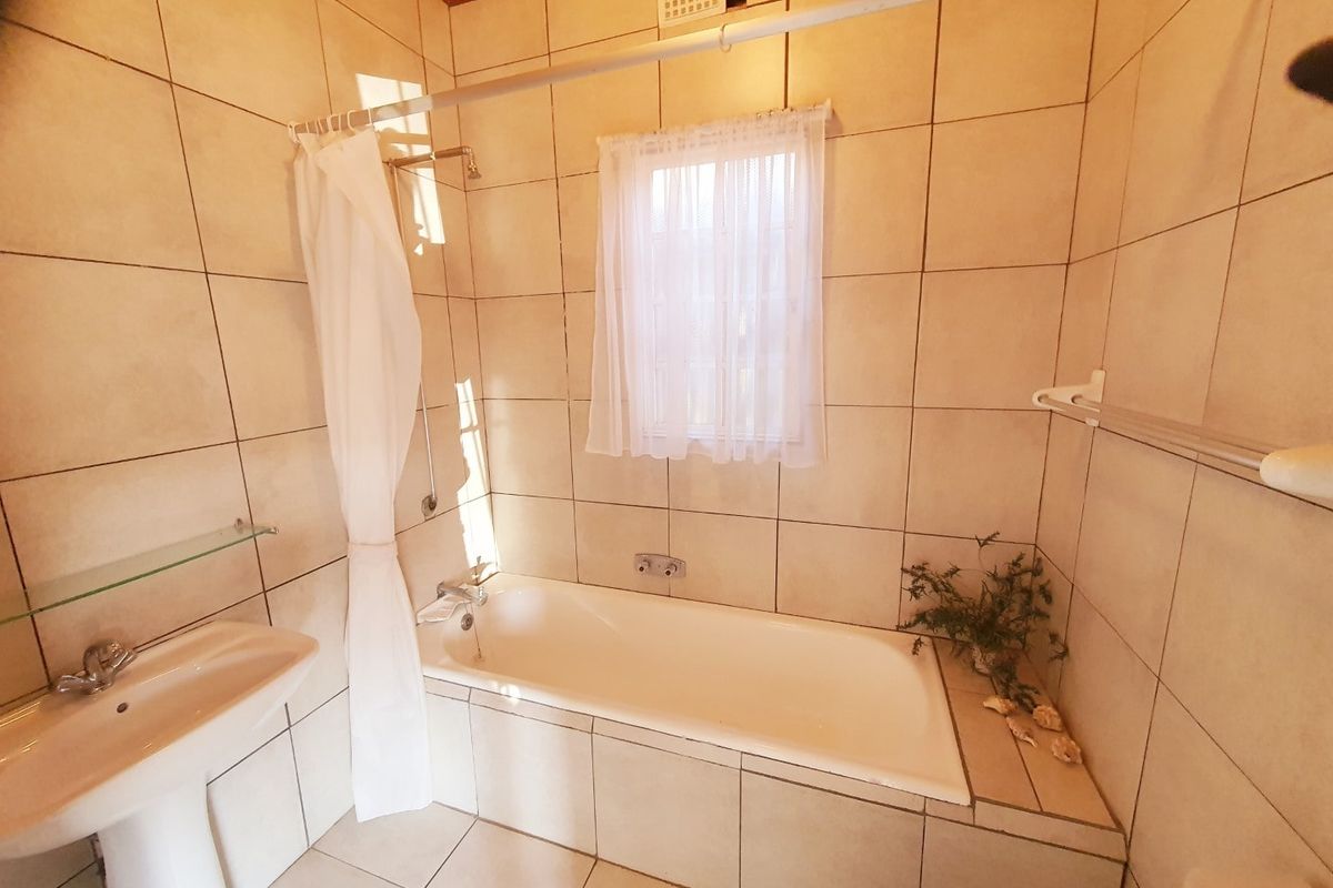 A functional bathroom featuring a pedestal basin, a built-in bathtub with shower mixer, and neutral wall and floor tiling.