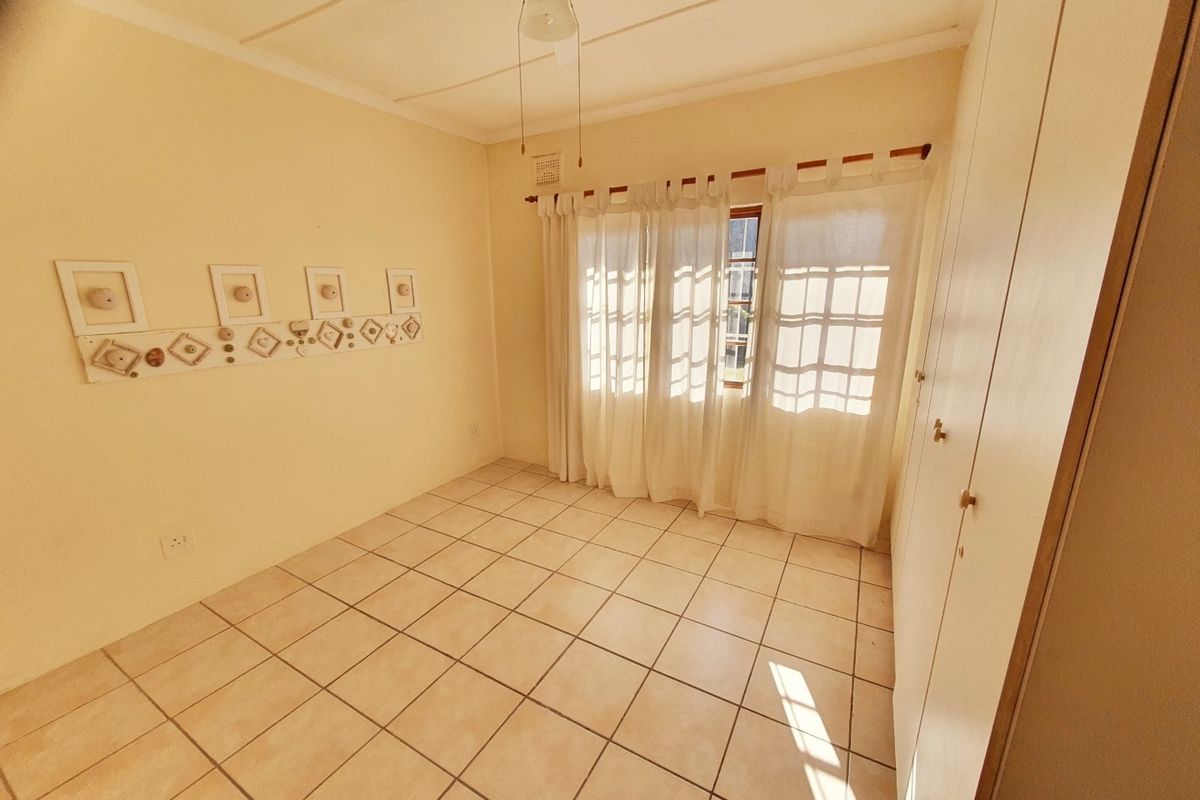 A bright, empty bedroom featuring tiled flooring, built-in cupboards, and a ceiling fan, offering a clean canvas for personalization.