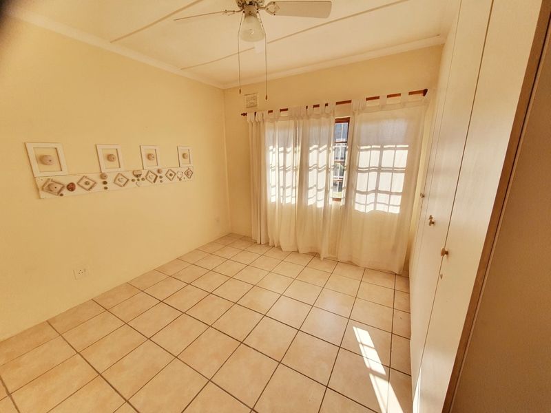 A bright, empty bedroom featuring tiled flooring, built-in cupboards, and a ceiling fan, offering a clean canvas for personalization.