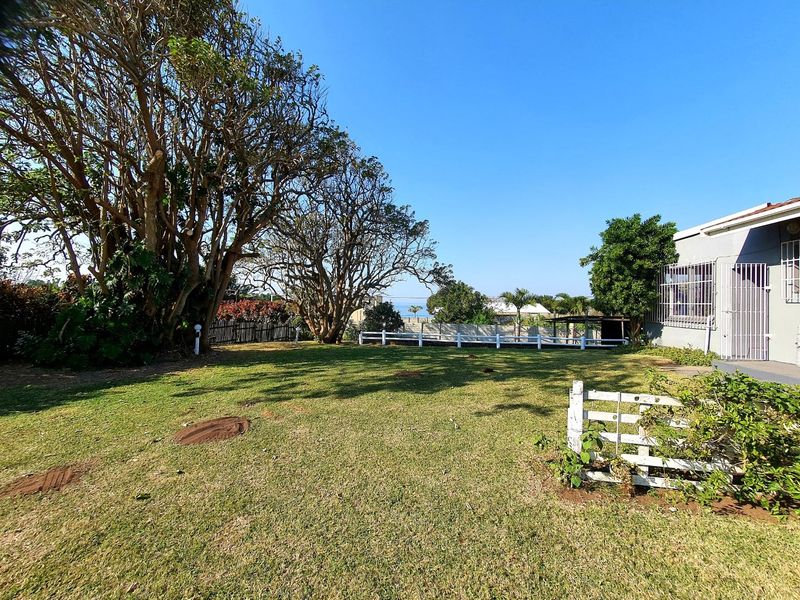 A spacious backyard garden featuring a well-maintained lawn, mature trees, and a white picket fence, offering a clear view of the surrounding area.