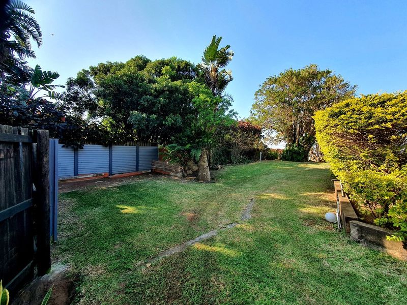 A spacious private garden featuring a well-maintained lawn, mature trees, and established boundary fencing, offering a peaceful outdoor setting.