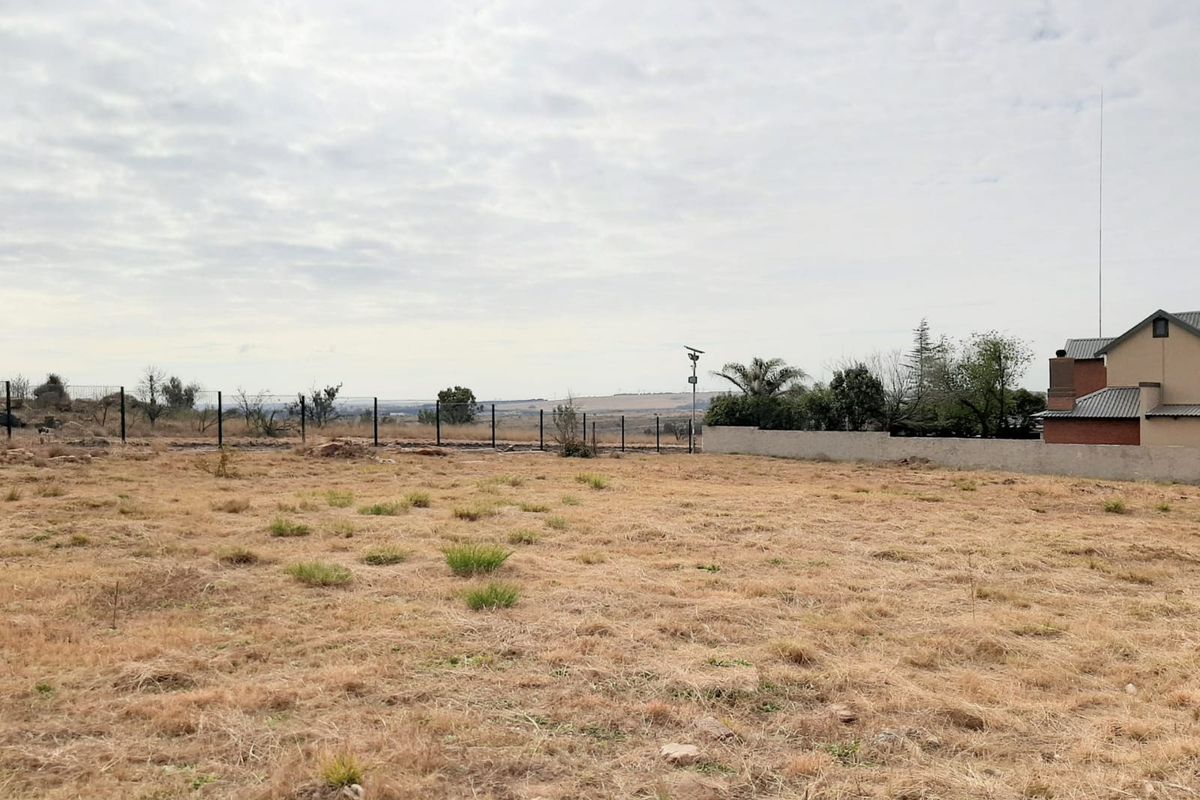 A vacant residential plot featuring perimeter fencing, a boundary wall, and open landscape views, ready for development.