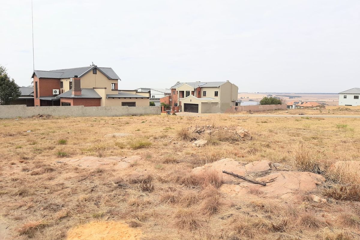A vacant residential plot featuring natural rocky terrain and surrounding boundary walls, situated in an established residential neighborhood.