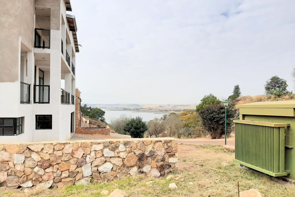 A scenic view overlooking a lake and surrounding landscape, featuring a modern multi-story building with balconies and a stone retaining wall.