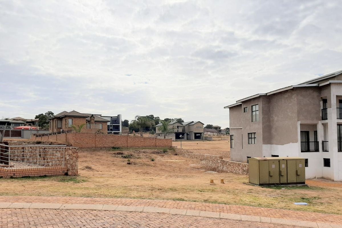 A vacant residential plot featuring a paved driveway, stone retaining wall, and brick boundary wall in a developing estate setting.