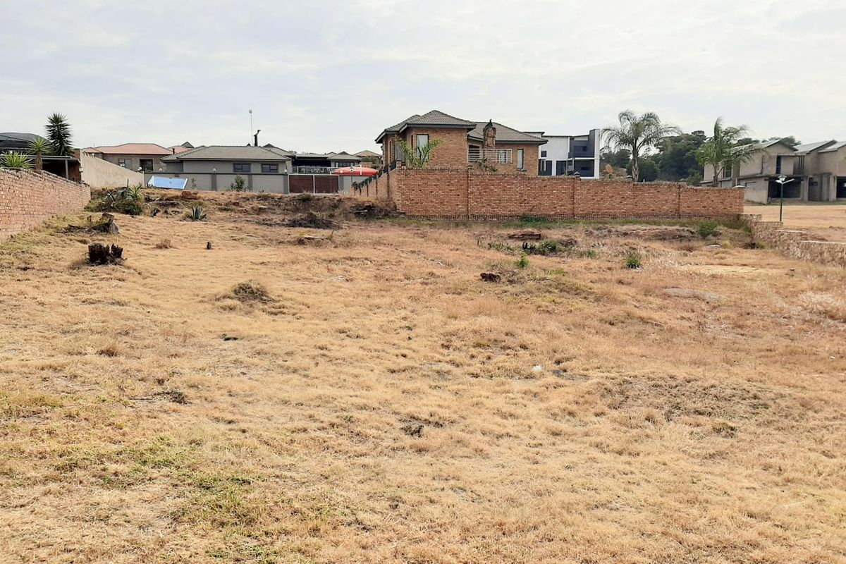 A vacant residential plot featuring a gentle slope and established brick boundary walls, situated in a developed neighborhood.