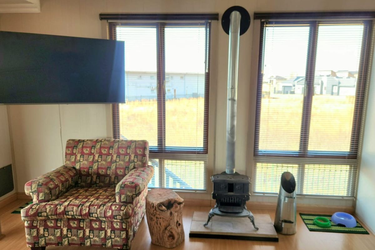 Living room featuring a freestanding wood-burning stove with a flue pipe, laminate flooring, and large windows with venetian blinds.