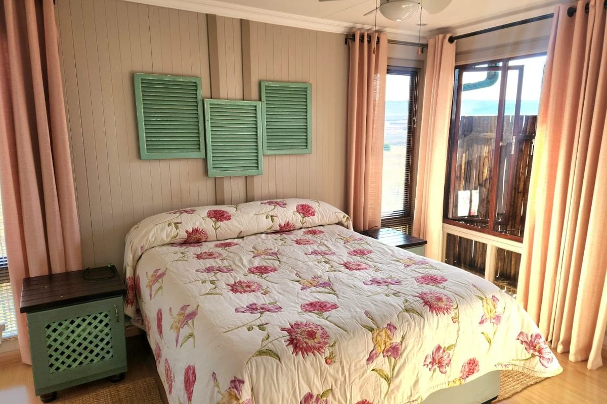 A cozy bedroom featuring timber wall paneling, a ceiling fan, and large windows that provide natural light and exterior views.