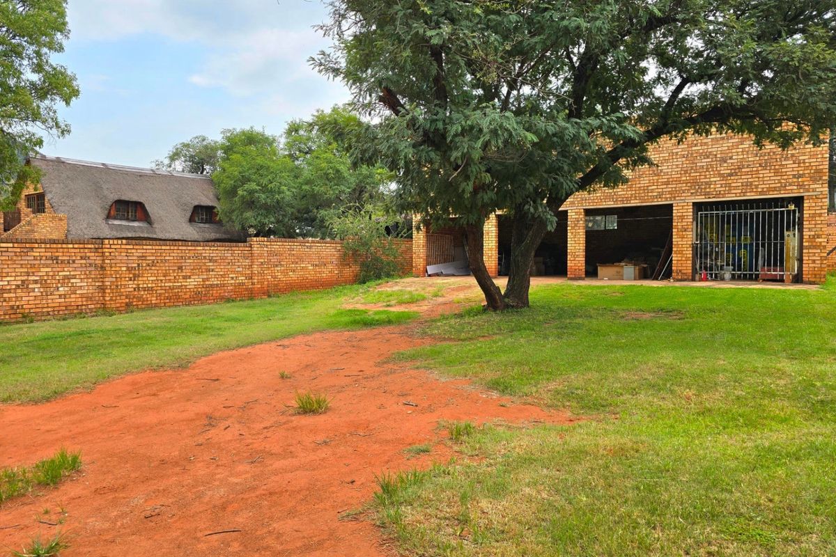 Spacious rear garden area featuring a brick boundary wall, mature trees, and a detached brick garage structure with metal security gates.