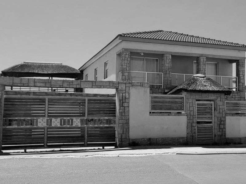 Front exterior view of a two-story house featuring stone cladding, a thatched roof, a balcony, and a secure gated entrance.