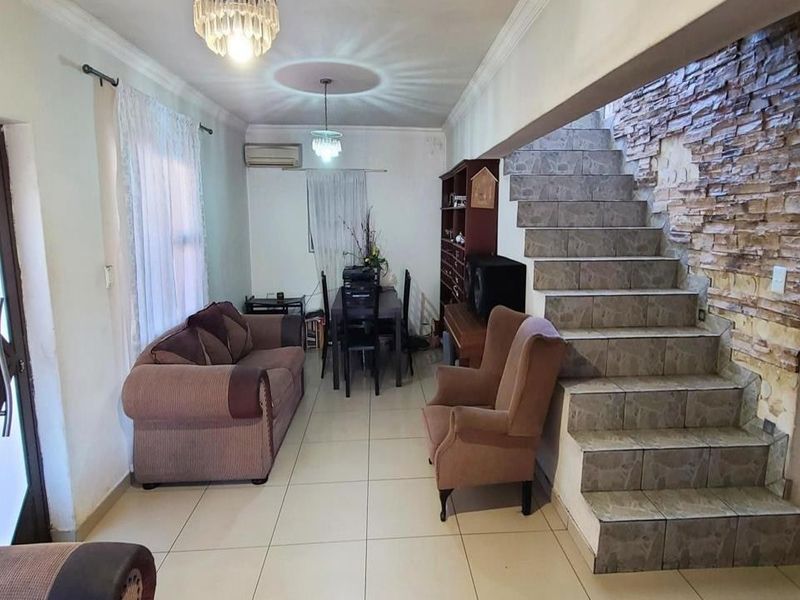 Open-plan living and dining area featuring tiled floors, a stone-clad feature wall, and a staircase leading to the upper level.
