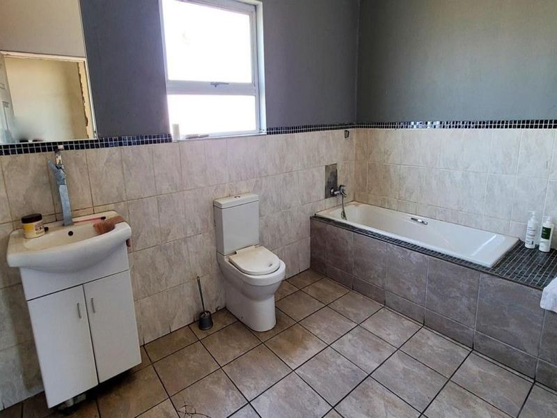 A functional bathroom featuring a built-in bathtub, pedestal basin, and toilet with neutral wall and floor tiling.