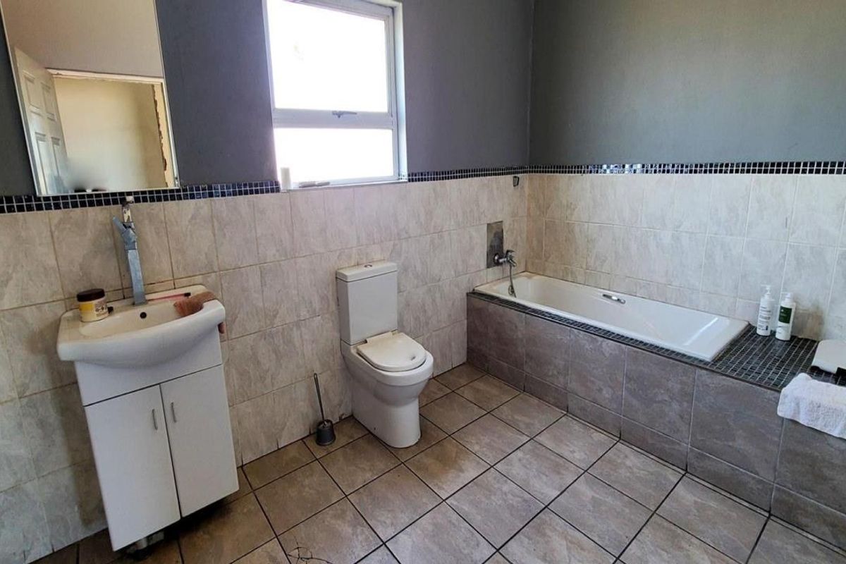 A functional bathroom featuring a built-in bathtub, pedestal basin, and toilet with neutral wall and floor tiling.
