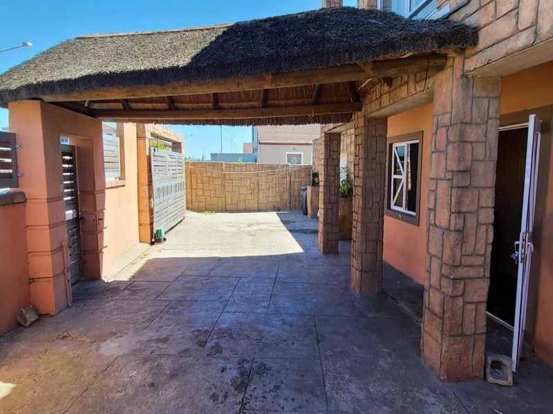Covered outdoor patio area featuring a thatched roof, stone-clad support pillars, and paved flooring, providing a functional space for outdoor living.