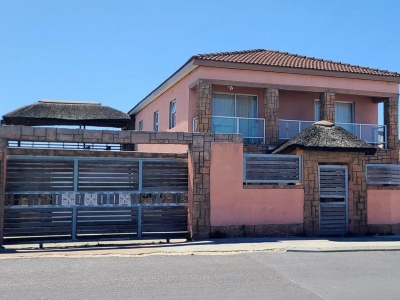 A two-story residential property featuring stone cladding, a tiled roof, a balcony, and a secure perimeter wall with sliding and pedestrian gates.